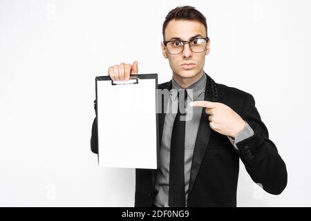 business man in suit, looks surprised, and hold a blank sheet of paper, and points his finger at him, on a white background Stock Photo