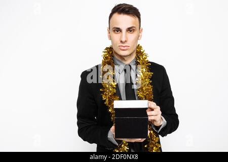 An elegant man in a black suit, and with tinsel on his neck, holding a black case, for decoration, a gift for the holiday, on a white background. blac Stock Photo
