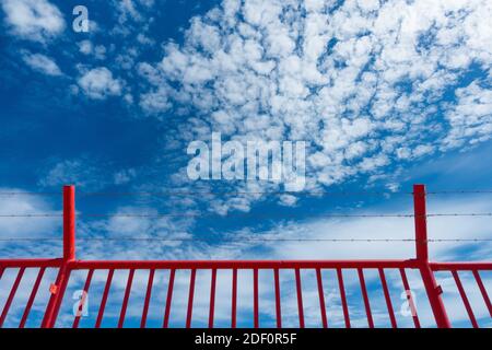 Red security fence topped with barbed wire/razor wire against blue sky. Stock Photo