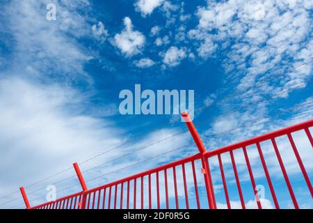 Red security fence topped with barbed wire/razor wire against blue sky. Stock Photo