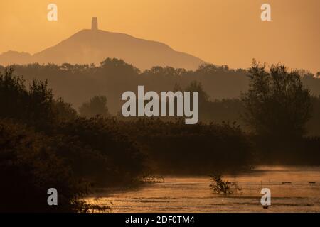 Autumn Equinox: Early morning light and mist over Glastonbury Tor in Somerset seen from Avalon marshes on the final day before summer officially ends. Stock Photo