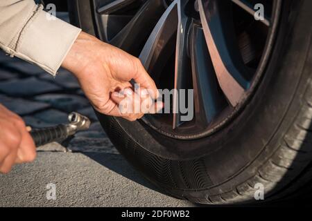 Close up of man hands inflating car tires. Tire air pressure checking before travel. Stock Photo