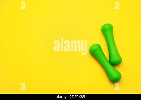 Green dumbbells lie on a yellow background. The concept of sport and a healthy lifestyle. Copy space, top view. Stock Photo