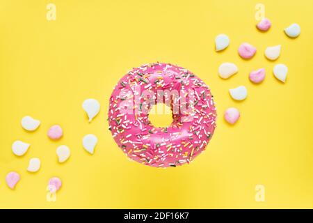 Sprinkled Pink Donut. Glazed sprinkled donut on bright yellow background with colorful candies. Top view, copy space Stock Photo