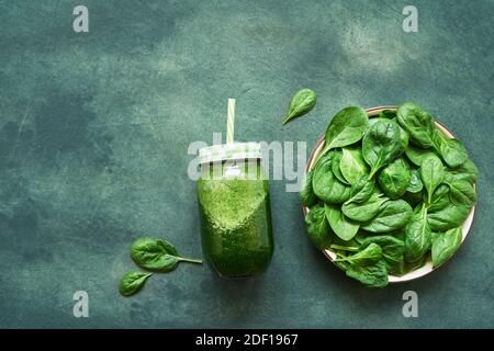 Green smoothie from spinach and kale in glass jar and plate with fresh spinach on green background. Healthy food flat lay. Copy space Stock Photo