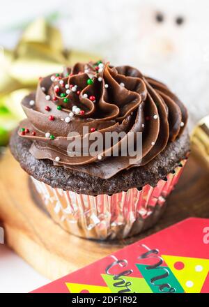 A Chocolate Christmas cupcake sits on a board surrounded by gift tag, bows, ornaments, and a Santa. Stock Photo