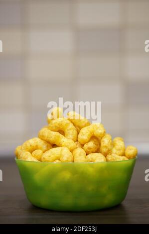 Many yellow corn puffs in a green bowl Stock Photo