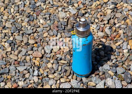 Blue tourist thermos made of metal, a little shabby stands on stones, pebbles. Stock Photo