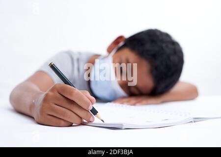 Schoolboy with protective face mask tired doing study and homework at home. new normal education concept Stock Photo
