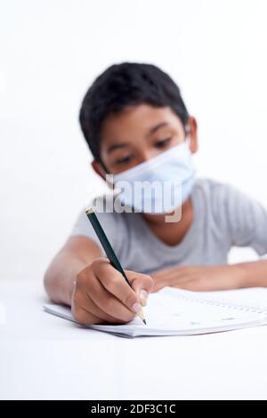 Schoolboy with protective face mask tired doing study and homework at home. new normal education concept Stock Photo