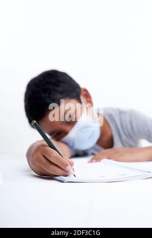 Schoolboy with protective face mask tired doing study and homework at home. new normal education concept Stock Photo