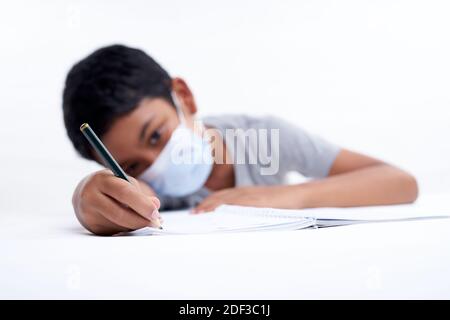 Schoolboy with protective face mask tired doing study and homework at home. new normal education concept Stock Photo