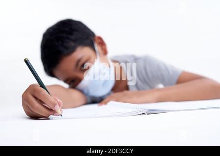 Schoolboy with protective face mask tired doing study and homework at home. new normal education concept Stock Photo