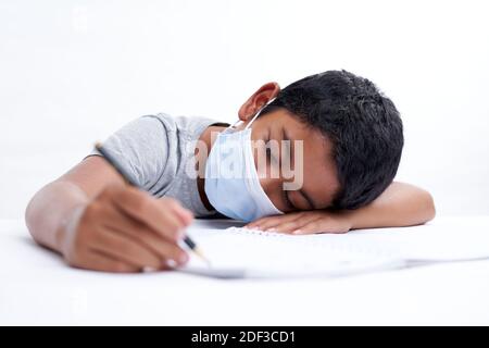 Schoolboy with protective face mask tired doing study and homework at home. new normal education concept Stock Photo