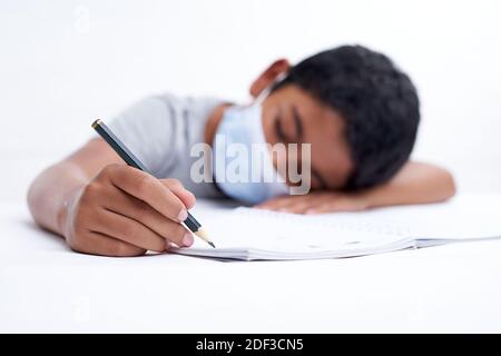 Schoolboy with protective face mask tired doing study and homework at home. new normal education concept Stock Photo