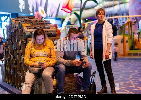 KOWNATY, POLAND - Jan 06, 2019: Woman and man sitting on a lumber shaped bench and using their smartphones in the Majaland Kownaty attraction park. Stock Photo