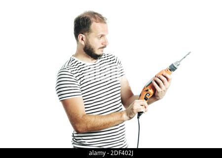 Mature bearded handyman looking at the drill machine in his hand with a questioning look Stock Photo