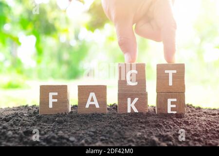 Fake news versus facts concept. Hand changing fake wooden blocks to word fact in natural background. Stock Photo