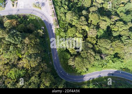 Aerial view drone shot top view of Asphalt road curve on mountain tropical rainforest with mountain peaks. Stock Photo