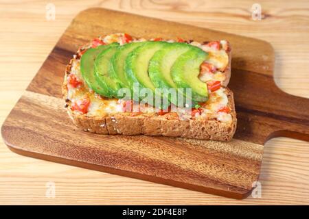 Closeup a homemade grilled cheese toast topped with tomato and sliced avocado on wooden Breadboard Stock Photo