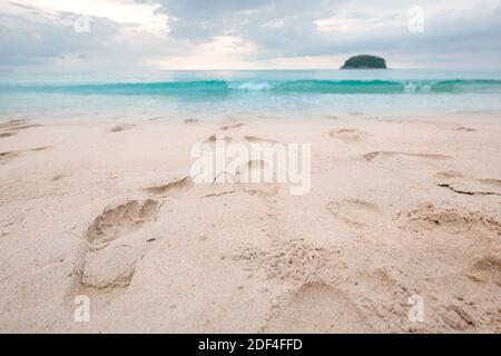 Footprints on beautiful sandy beach and turquoise sea water at sunset time. Stock Photo