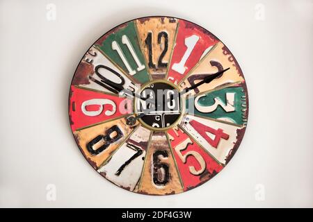 The clock with vintage metal face on white wall, referring to design of 1930s-50s, with digits and sectors of different colors Stock Photo