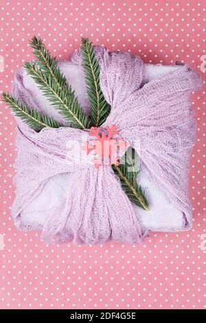 gift wrapped in pink textile with fir branches on red background. Christmas celebration zero waste concept. Stock Photo