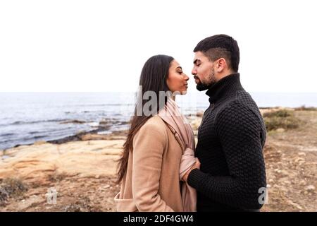 Young beautiful mixed race heterosexual lovers couple look at each other in their eyes face-to-face just before kissing outdoor on the seaside - Hands Stock Photo
