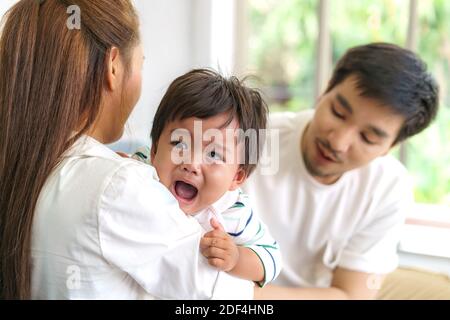 Asian Parents with mother and father trying to calm down crying infant son in living room at home Stock Photo