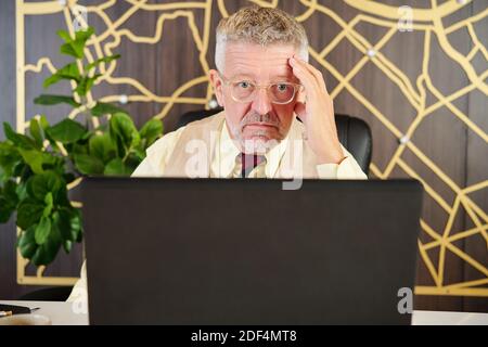 Shoked senior businessman reading report or contract on laptop screen in modern office Stock Photo