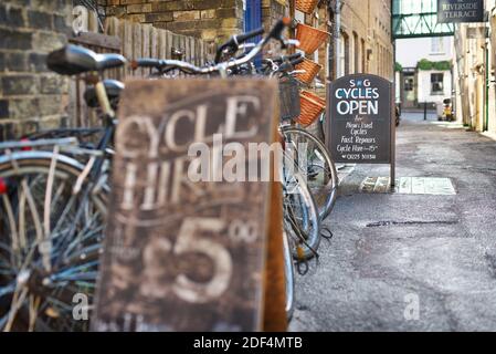 Cobbled streets in Cambridge, UK with cycle hire signs and tourists and locals going about their daily business on cycles Stock Photo