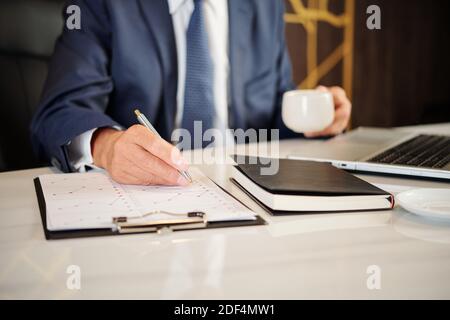 Close-up image of businessman having cup of coffee when analyzing financial statistics in report Stock Photo