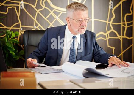 Serious head of roads and buildings department checking construction plans on his table Stock Photo