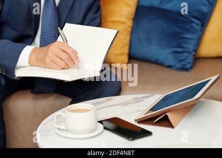 Close-up image of entrepreneur having online conference with colleagues and taking notes in planner Stock Photo
