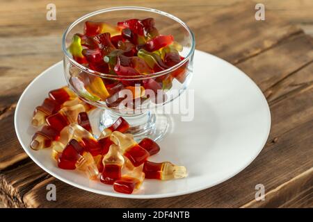 Chewing marmalade bottles of cola and bears on white plate on wooden background Stock Photo