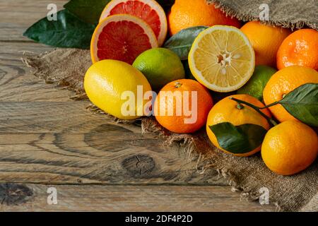 Assortment of citrus fruits in rustic style, Oranges, grapefruits, lemons and limes on burlap on wooden background. Stock Photo
