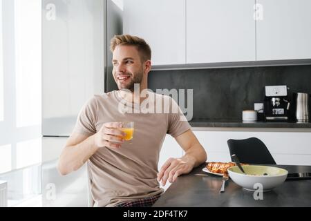 Young handsome caucasian man smiling while having breakfast at home Stock Photo