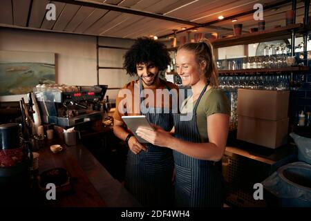 Smiling waiter and waitress wearing apron using digital tablet standing behind counter in cafe Stock Photo
