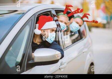 Friends wearing a protective face mask in the car. Holidays during epidemic. Stock Photo