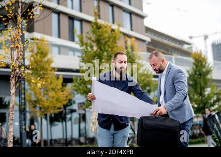 Two young engineers checking the architectural plan outdoors Stock Photo
