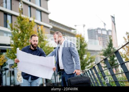 Two young engineers checking the architectural plan outdoors Stock Photo