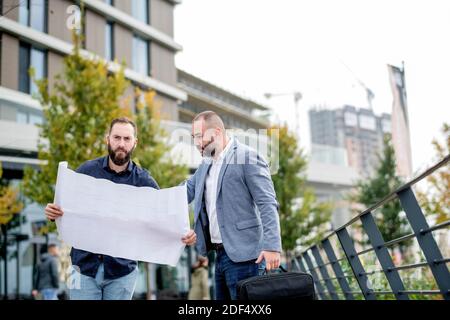 Two young engineers checking the architectural plan outdoors Stock Photo