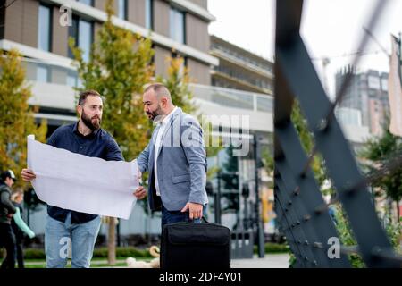 Two young engineers checking the architectural plan outdoors Stock Photo