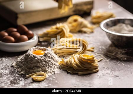 Nests of fresh fettuccine pasta with eggs, egg yolk, flour on a kitchen prep table. Stock Photo