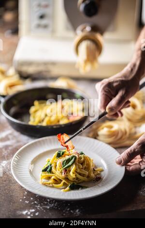 Hands of chef plating freshly cooked pasta with a pasta maker in the background. Stock Photo