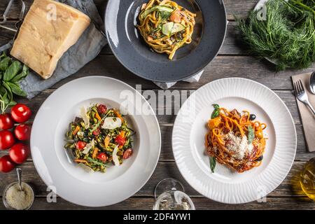 Top view of various pasta dishes served on plates, surrounded by ingredients on a vintage wooden surface. Stock Photo