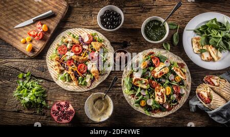 Top view of open tortillas with vegetables and chicken strips or haloumi cheese on a rustic table. Stock Photo