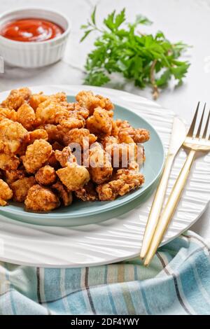 Popcorn chicken - american fast food dish of bite-sized chicken pieces breaded and fried, served on a white plate with ketchup and golden fork on a wh Stock Photo
