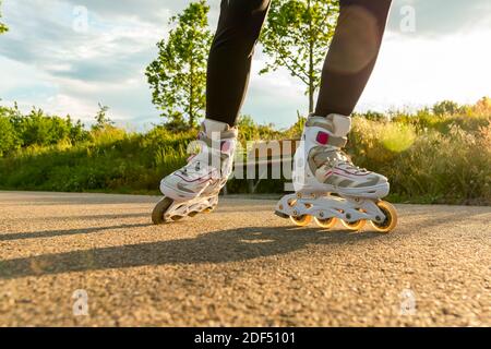 Close-up shot of white Inline skates on the path. Woman's legs with roller blades at sunny day. Stock Photo