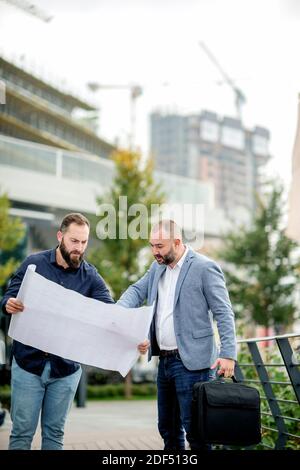 Two young engineers checking the architectural plan outdoors Stock Photo